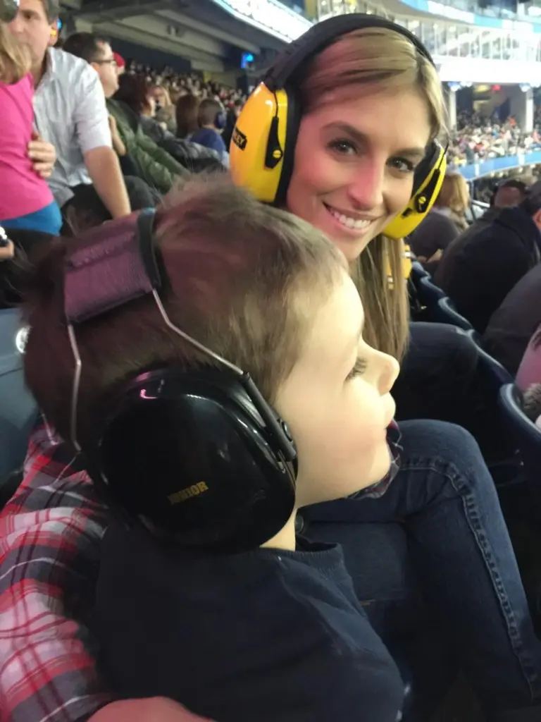 Families wearing earmuffs and sun protection at loud dirt-track event.