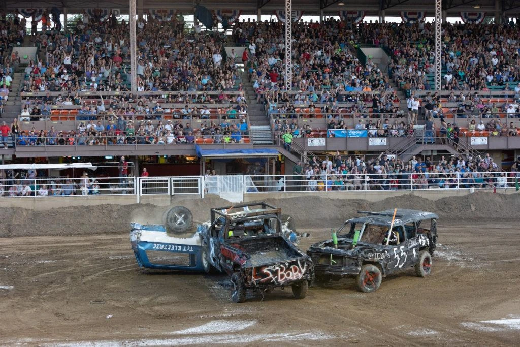 Demolition derby cars crashing on muddy dirt track at night.
