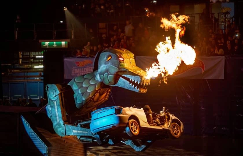 Illuminated Hot Wheels monster trucks and fire-breathing dinosaur during arena show.