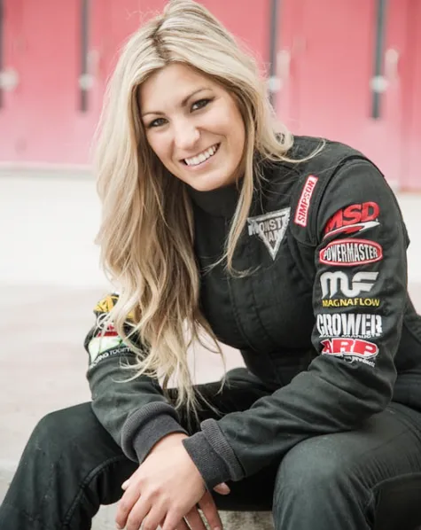 A woman in a racing suit sitting on a ledge