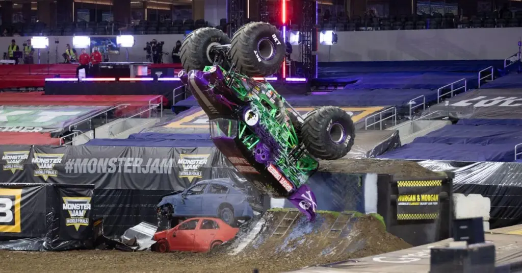 Monster trucks racing, wheelie competitions, and freestyle jumps on dirt track.